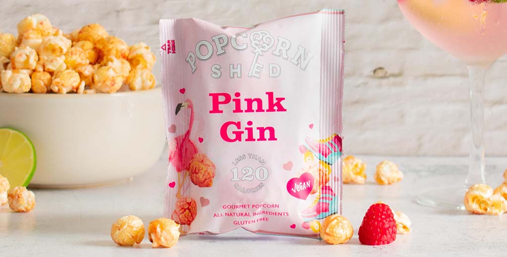 A Pink Gin popcorn snack pack surrounded by caramel coated popcorn kernels and fresh fruit; a perfect summer snack. 
