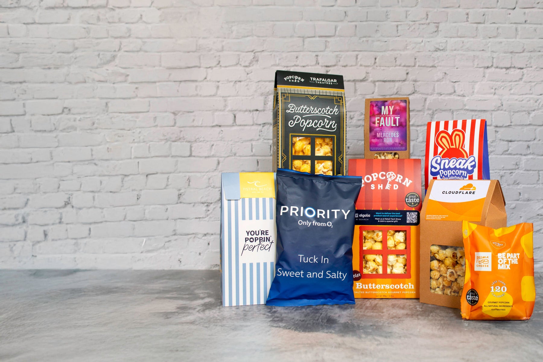 Assorted popcorn packages on a gray surface with a white brick wall background