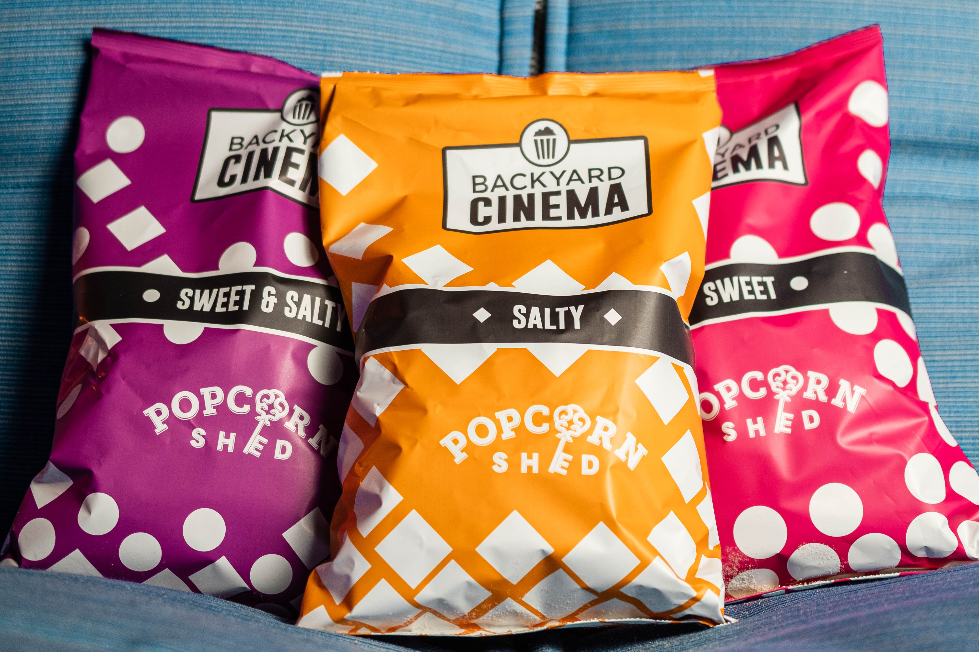 Three bags of Backyard Cinema popcorn on a blue couch.