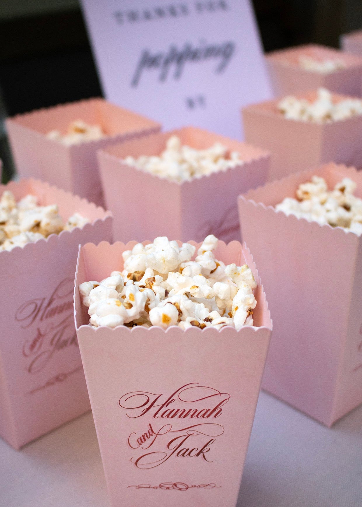 Pink popcorn boxes with 'Hannah and Jack' text, filled with popcorn, on a table.